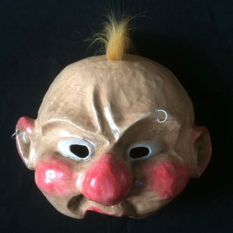 Demi-masque en papier mâché représentant un visage avec des piercings et une touffe de cheveux blonds