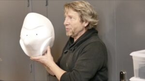 Sydney Bernard tenant un masque larvaire créé par Pierre Filliez dans ses mains