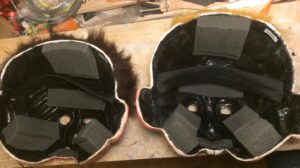 Vue intérieure de deux masques en papier mâché. On voit les mousses de rembourrage, les élastiques et la peinture noire.